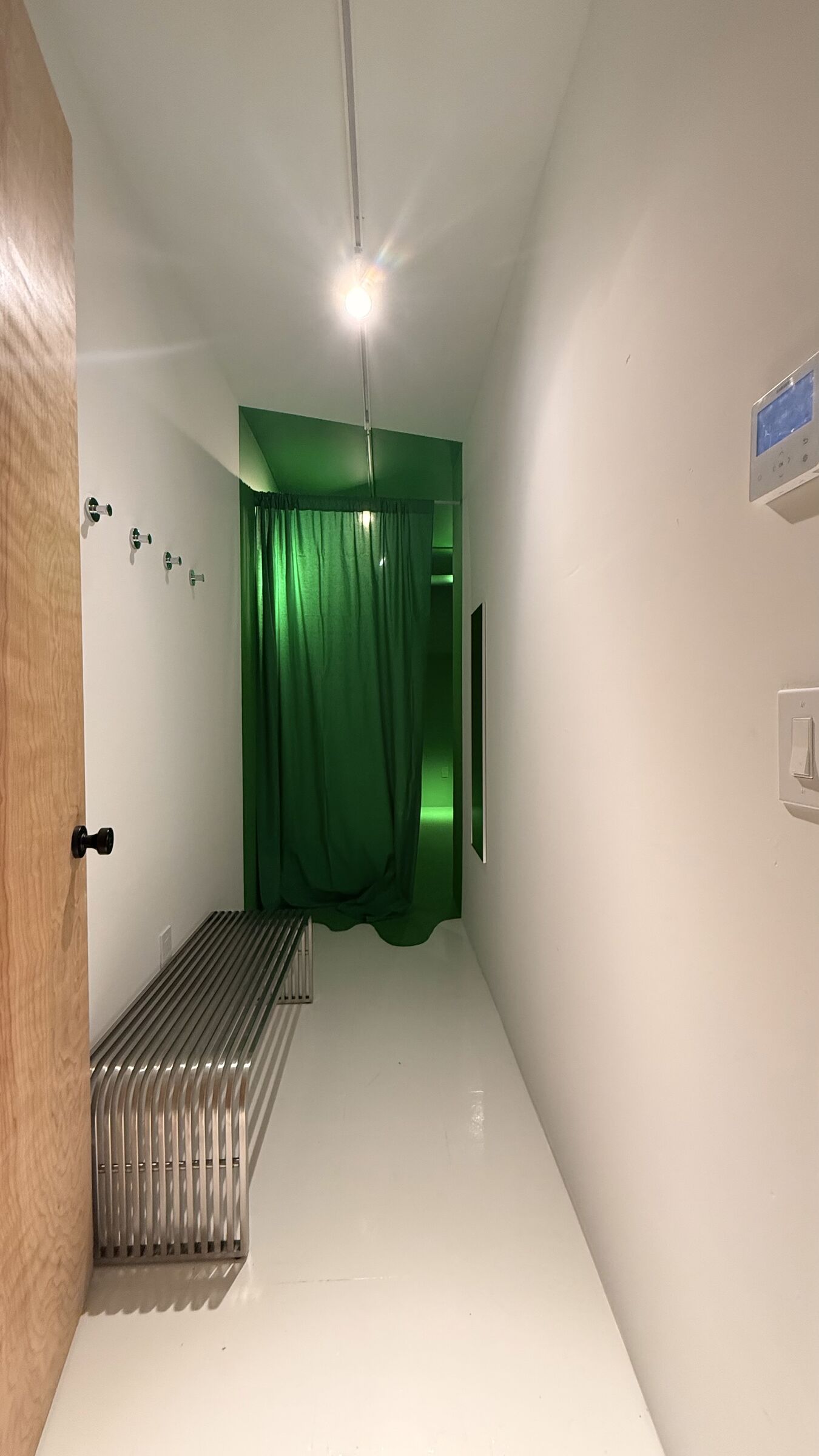 The Stage — a green-screen chamber framed through the doorway, stainless bench in the white anteroom, green curtain pulled back to reveal the chroma alcove